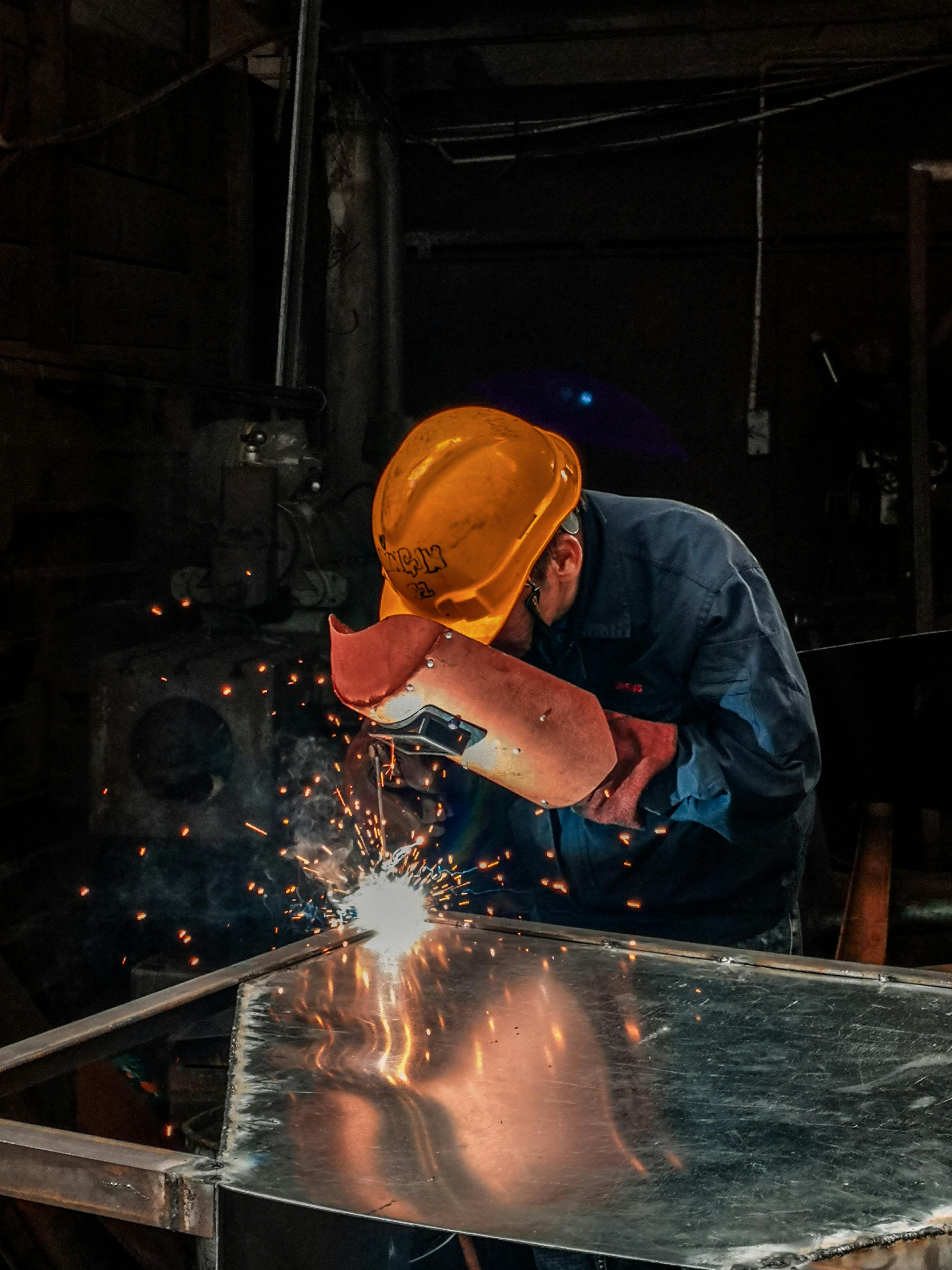 pexels-photo-2480481-2480481 A welder wearing protective gear works on metal in an industrial workshop, surrounded by sparks.