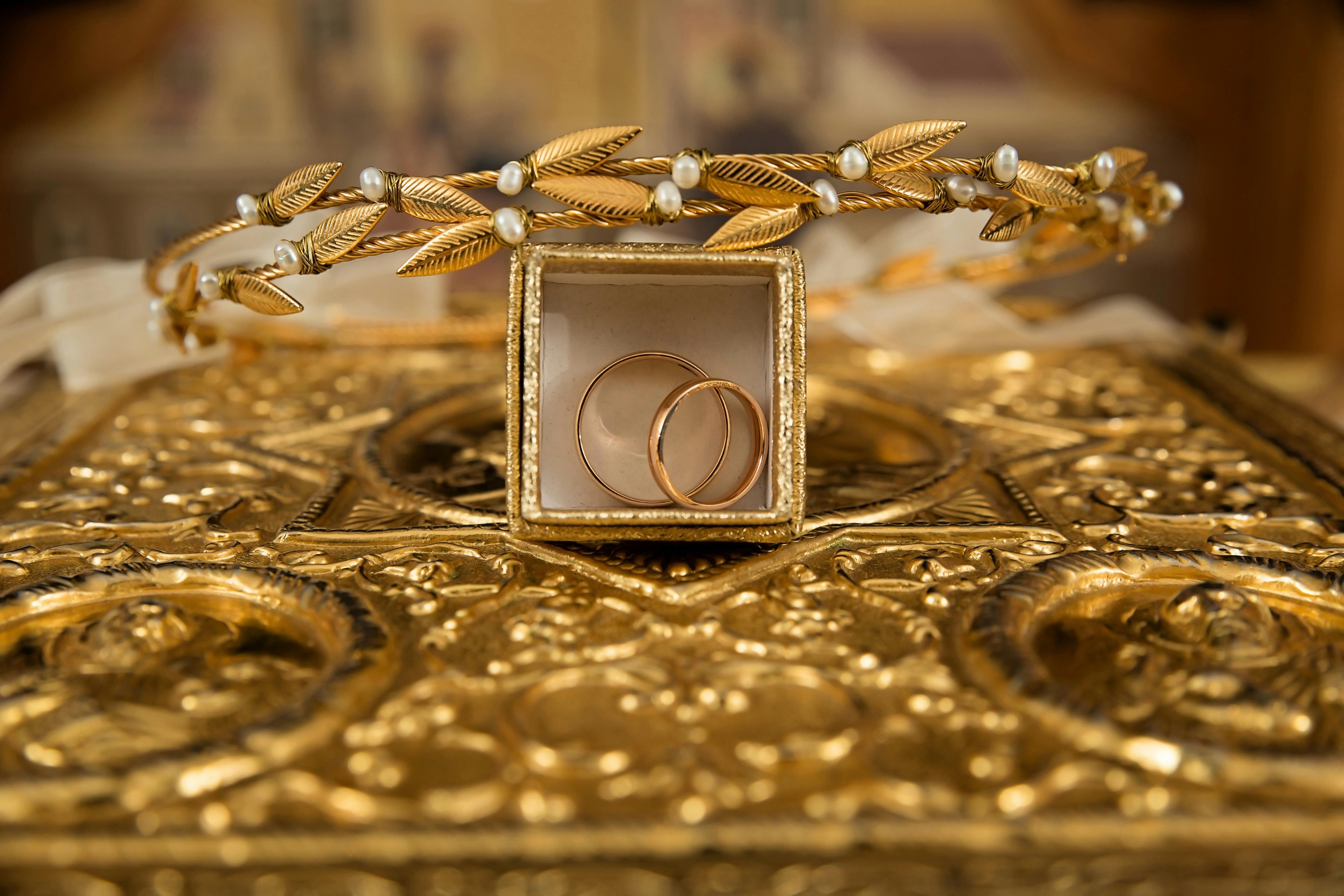 pexels-photo-248077-248077 Close-up of gold wedding rings and a delicate tiara on an ornate golden background, symbolizing luxury and elegance.