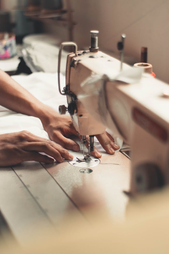 pexels-photo-2973392 Close-up of hands using a sewing machine, depicting craftsmanship and textiles indoors.