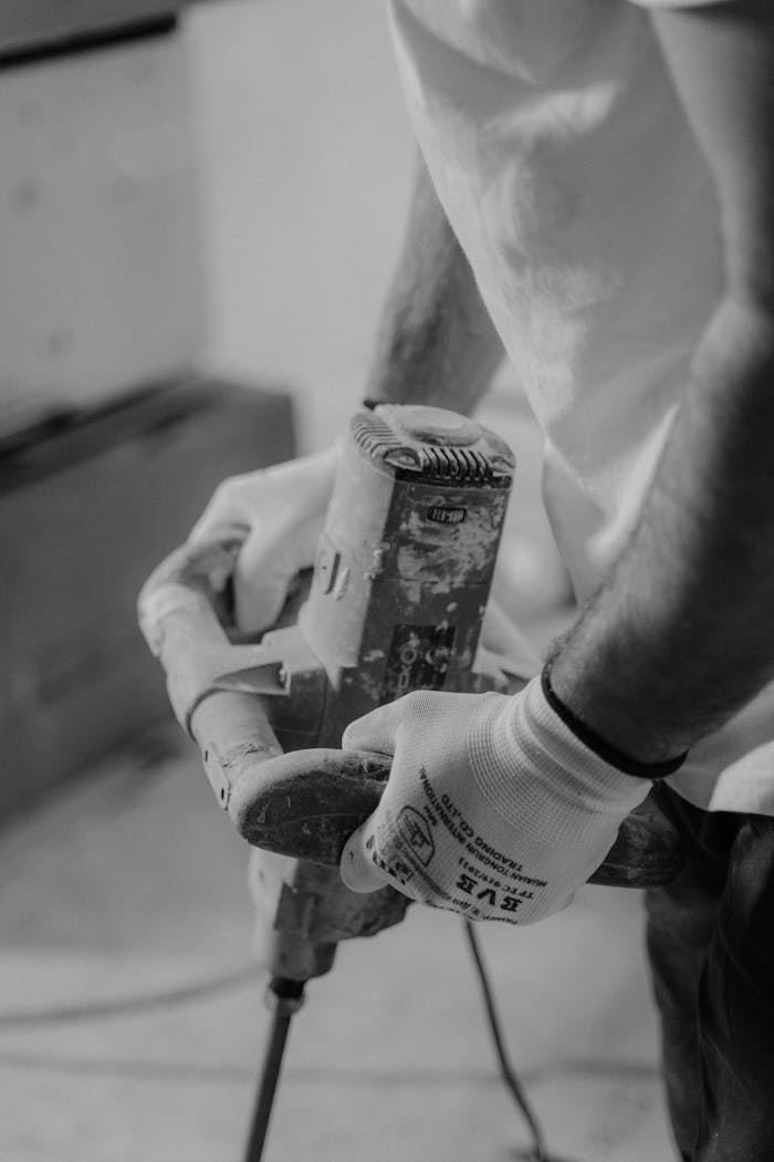 pexels-photo-6474194 Close-up of a man using a hand drill in a carpentry workshop. Black-and-white image emphasizing craftsmanship.