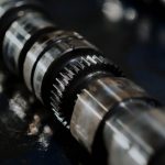 Detailed image of a camshaft showcasing gears and reflections on a dark surface.